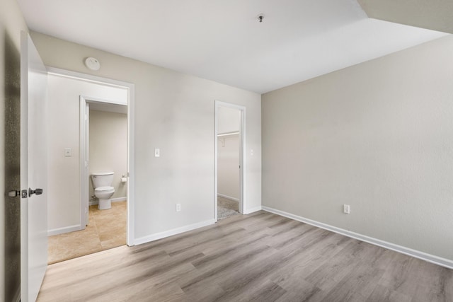 unfurnished bedroom featuring ensuite bath, a spacious closet, a closet, and light hardwood / wood-style flooring