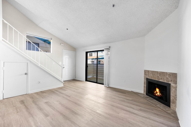 unfurnished living room with a tile fireplace, a textured ceiling, light wood-type flooring, and lofted ceiling