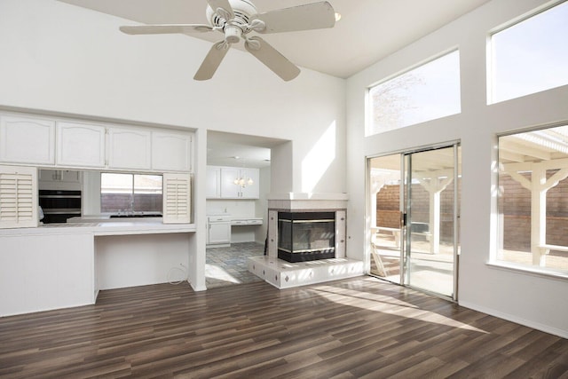 unfurnished living room featuring a high ceiling, ceiling fan with notable chandelier, and dark hardwood / wood-style flooring