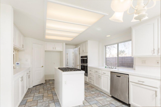 kitchen with sink, tile countertops, a kitchen island, stainless steel appliances, and white cabinets