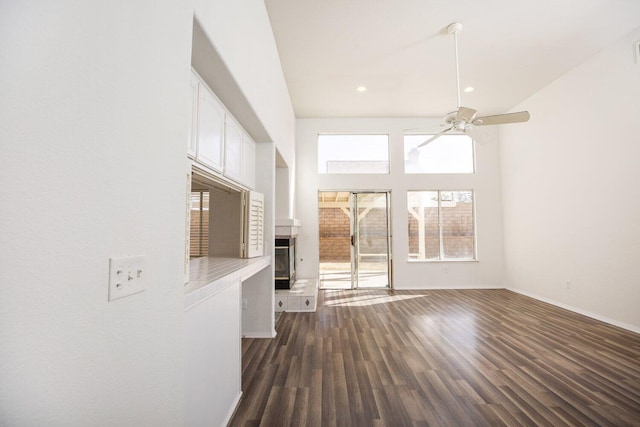 unfurnished living room with a high ceiling, dark wood-type flooring, and ceiling fan