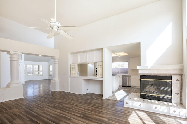 unfurnished living room featuring a tiled fireplace, dark wood-type flooring, decorative columns, and ceiling fan