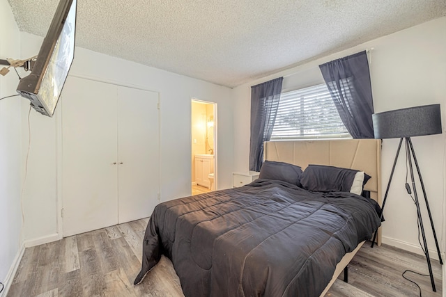 bedroom with connected bathroom, light hardwood / wood-style floors, and a textured ceiling