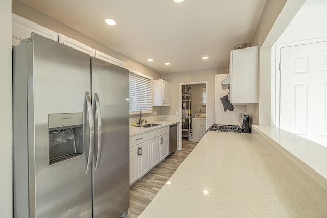 kitchen with sink, light hardwood / wood-style flooring, ventilation hood, white cabinets, and appliances with stainless steel finishes