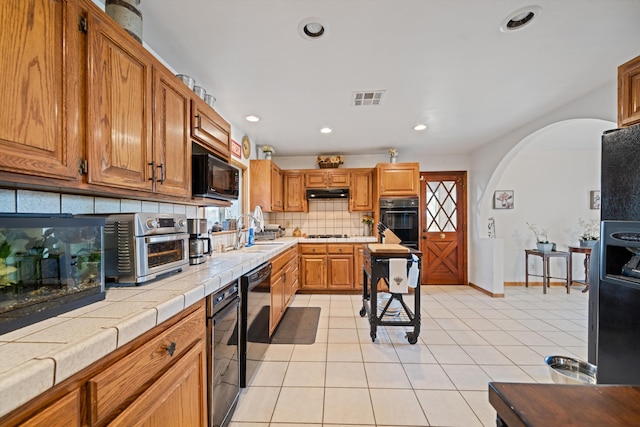 kitchen with arched walkways, under cabinet range hood, a sink, visible vents, and black appliances