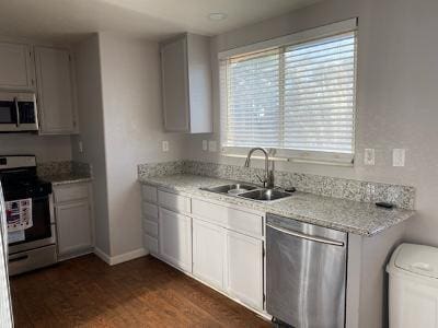 kitchen with light stone countertops, appliances with stainless steel finishes, dark wood-type flooring, sink, and white cabinets