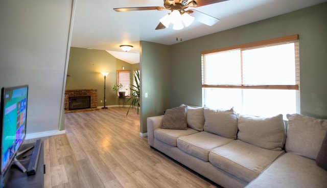 living room featuring light wood finished floors, lofted ceiling, a glass covered fireplace, ceiling fan, and baseboards