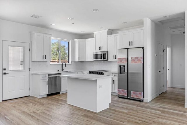 kitchen featuring appliances with stainless steel finishes, light wood-type flooring, sink, a center island, and white cabinetry