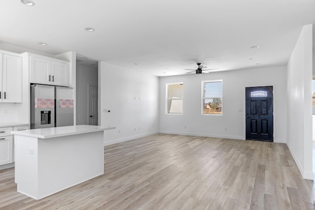 kitchen with stainless steel fridge, ceiling fan, white cabinets, a center island, and light hardwood / wood-style floors