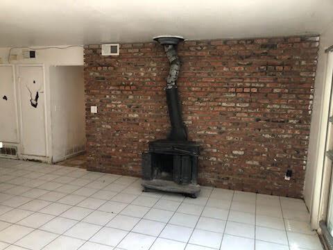 1132 Morven St, Lancaster, CA 93535 - unfurnished living room with a wood stove, brick wall, and light tile patterned flooring