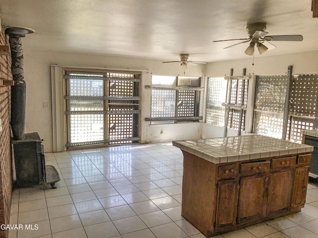 1132 Morven St, Lancaster, CA 93535 - kitchen with a wood stove, tile countertops, a ceiling fan, light tile patterned floors, and brown cabinetry