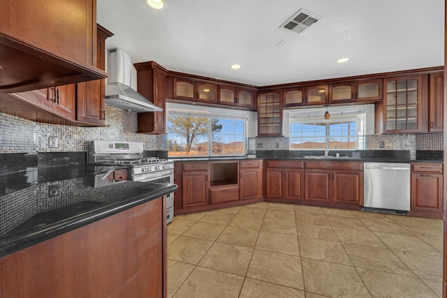 kitchen featuring stainless steel appliances, a sink, visible vents, wall chimney range hood, and decorative backsplash