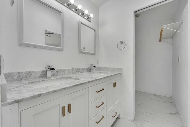 full bathroom with double vanity, marble finish floor, baseboards, and a sink