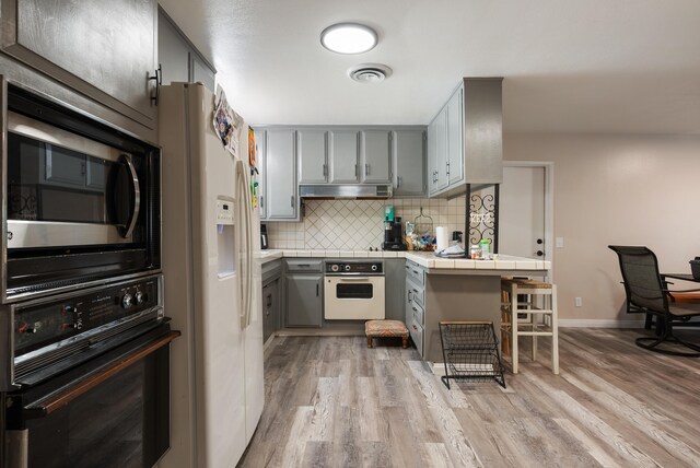43818 Halcom Ave, Lancaster, CA 93536 - kitchen featuring white appliances, gray cabinetry, under cabinet range hood, and tile countertops