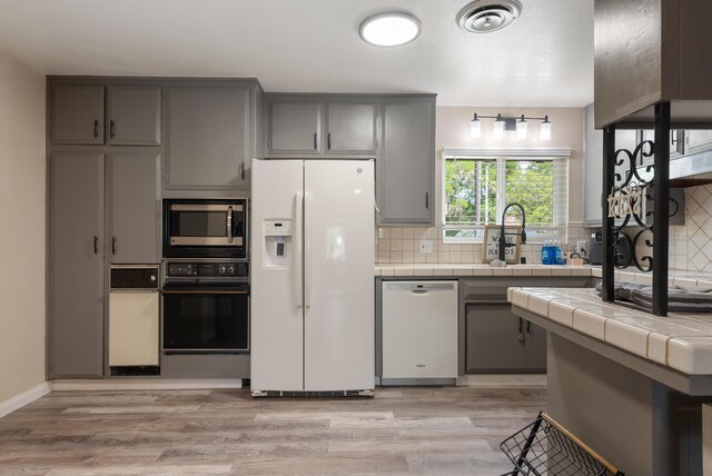 43818 Halcom Ave, Lancaster, CA 93536 - kitchen featuring white appliances, gray cabinetry, tile countertops, decorative backsplash, and light wood finished floors