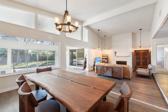 dining area featuring beam ceiling, a chandelier, wood finished floors, a textured ceiling, and a brick fireplace