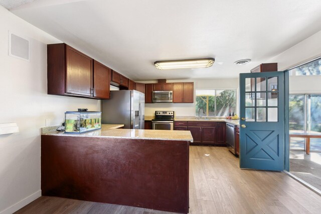 kitchen with a peninsula, appliances with stainless steel finishes, light wood-style floors, and visible vents