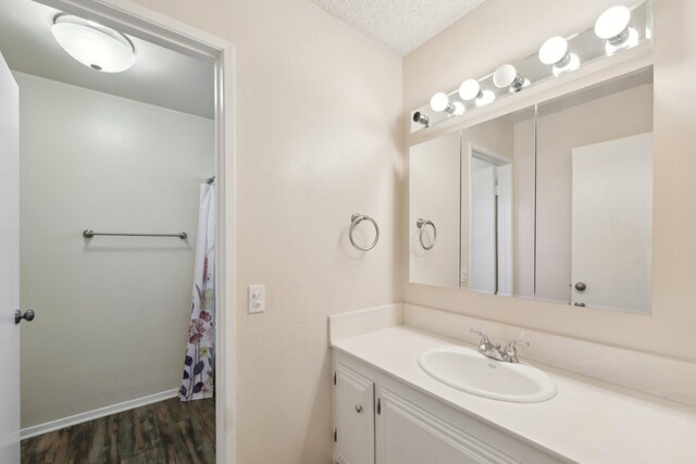 bathroom with baseboards, a textured ceiling, wood finished floors, and vanity