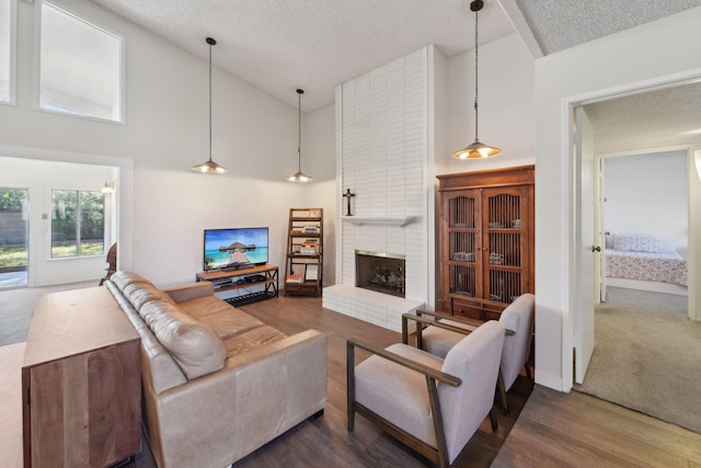 living room featuring a fireplace, a textured ceiling, high vaulted ceiling, and wood finished floors