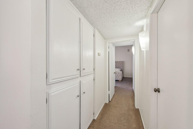 hallway with a textured ceiling and light colored carpet