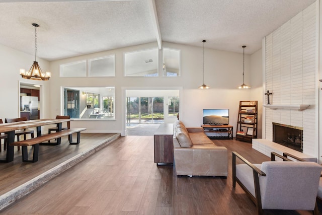 living area featuring dark wood-style flooring, a textured ceiling, beam ceiling, a brick fireplace, and a notable chandelier