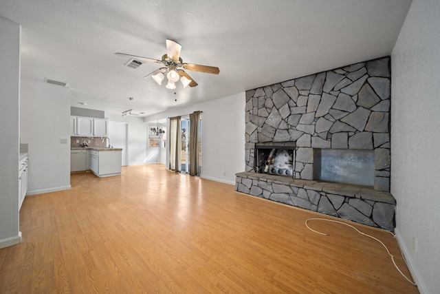 unfurnished living room featuring light wood-type flooring, visible vents, ceiling fan, and a stone fireplace