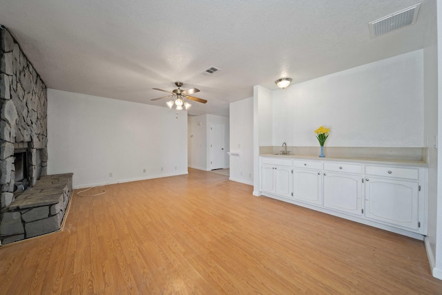 unfurnished living room with visible vents, light wood-style flooring, ceiling fan, a stone fireplace, and a sink