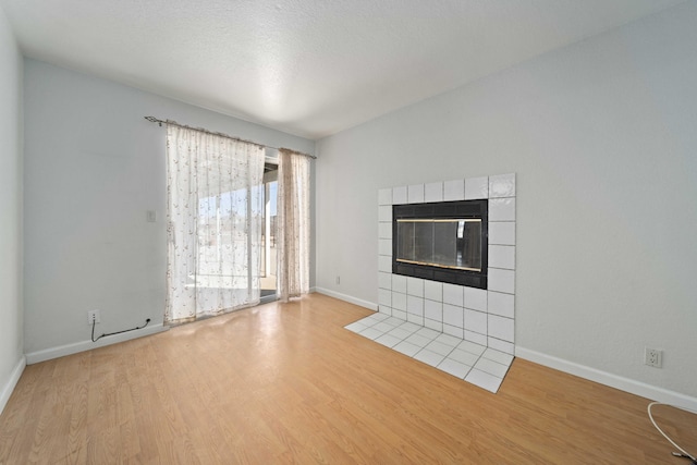 unfurnished living room with a textured ceiling, a tiled fireplace, baseboards, and wood finished floors