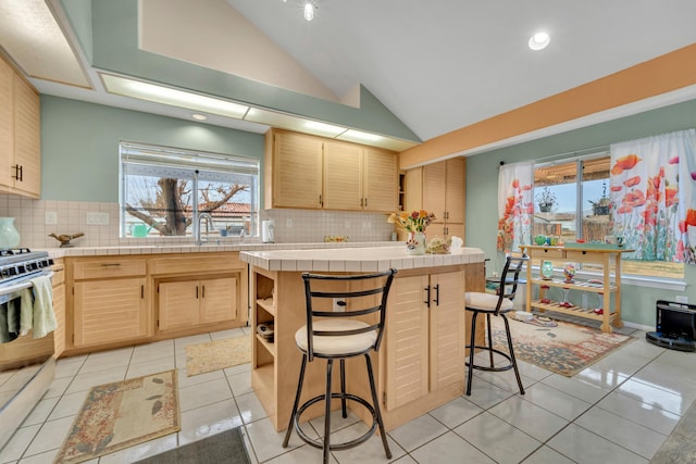 kitchen with stainless steel gas range oven, open shelves, tile countertops, light tile patterned flooring, and vaulted ceiling