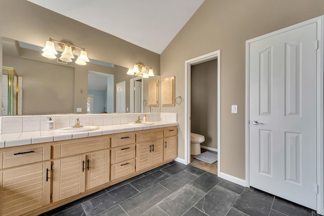 full bath featuring baseboards, toilet, lofted ceiling, double vanity, and a sink