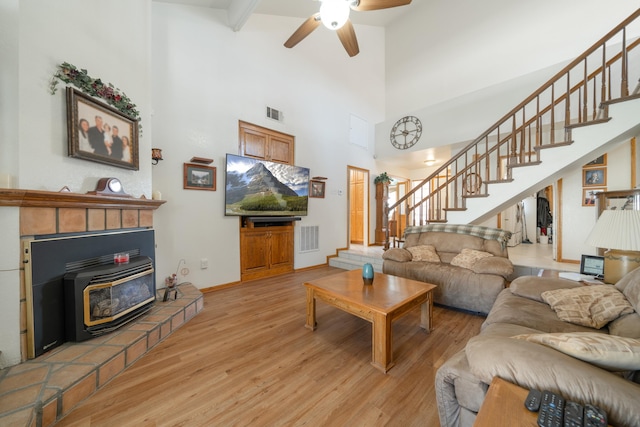 living room with beam ceiling, ceiling fan, a towering ceiling, and light wood-type flooring