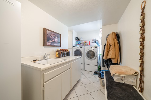 clothes washing area featuring sink, cabinets, washing machine and dryer, a textured ceiling, and light tile patterned flooring