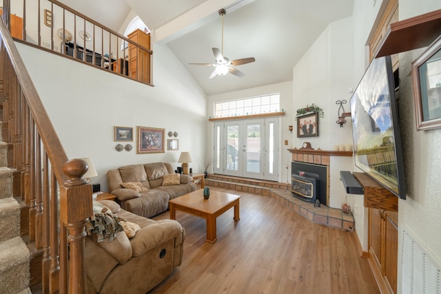 living room with ceiling fan, beam ceiling, high vaulted ceiling, light hardwood / wood-style flooring, and a wood stove