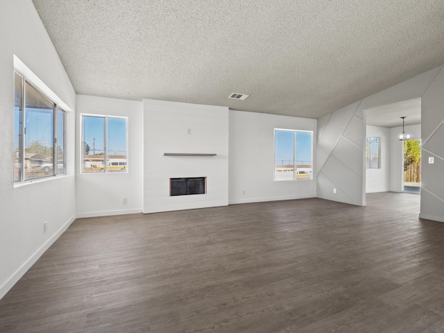 unfurnished living room with a chandelier, a textured ceiling, a large fireplace, and dark wood-type flooring