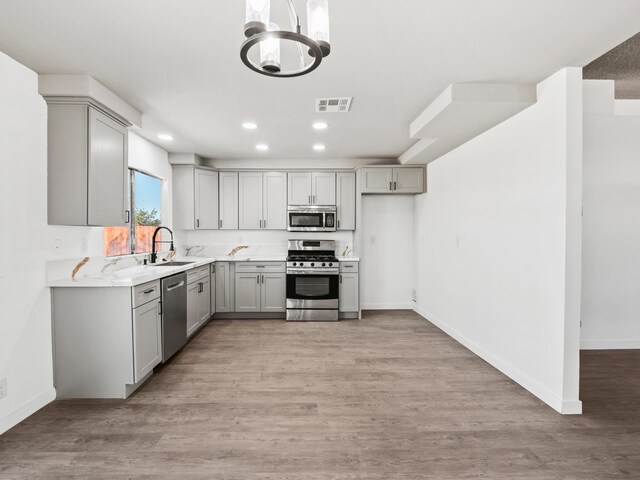 kitchen featuring sink, stainless steel appliances, light stone counters, light hardwood / wood-style floors, and gray cabinets