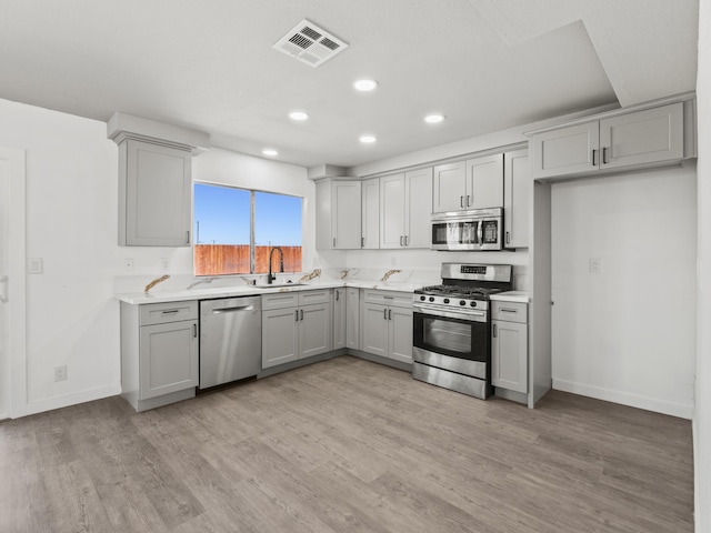 kitchen featuring light stone countertops, appliances with stainless steel finishes, gray cabinetry, sink, and light hardwood / wood-style flooring