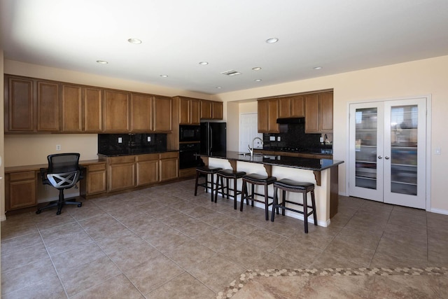 kitchen featuring french doors, a breakfast bar, a kitchen island with sink, black appliances, and light tile patterned floors