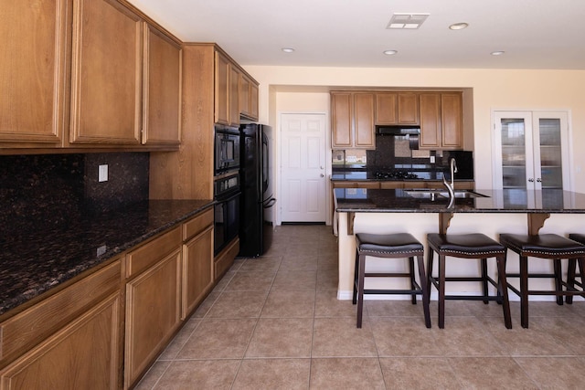 kitchen featuring light tile patterned floors, dark stone counters, black appliances, and sink