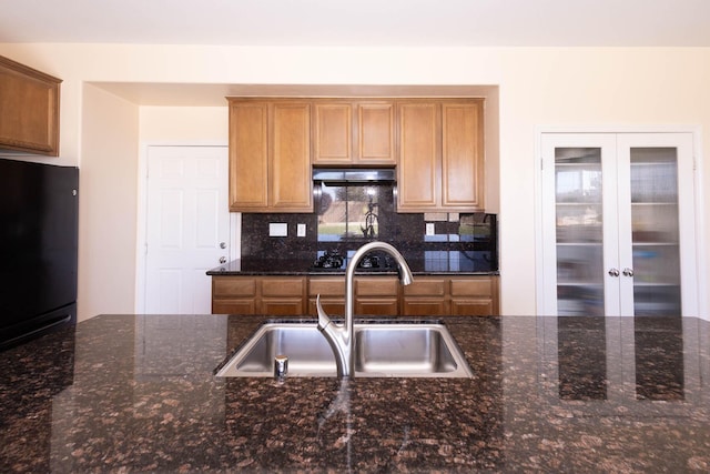 kitchen with black refrigerator, french doors, backsplash, dark stone counters, and sink