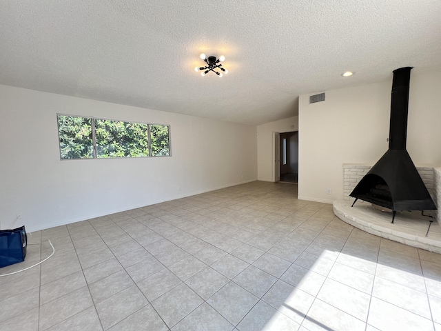 unfurnished living room with a textured ceiling, a wood stove, and light tile patterned flooring