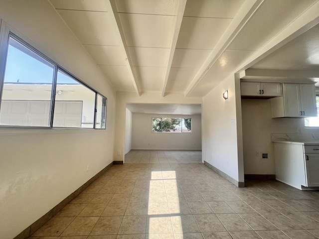 empty room featuring beamed ceiling and light tile patterned floors