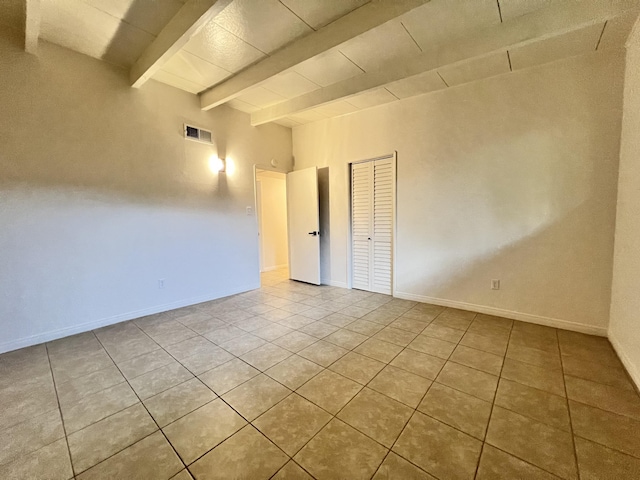 tiled empty room featuring beam ceiling