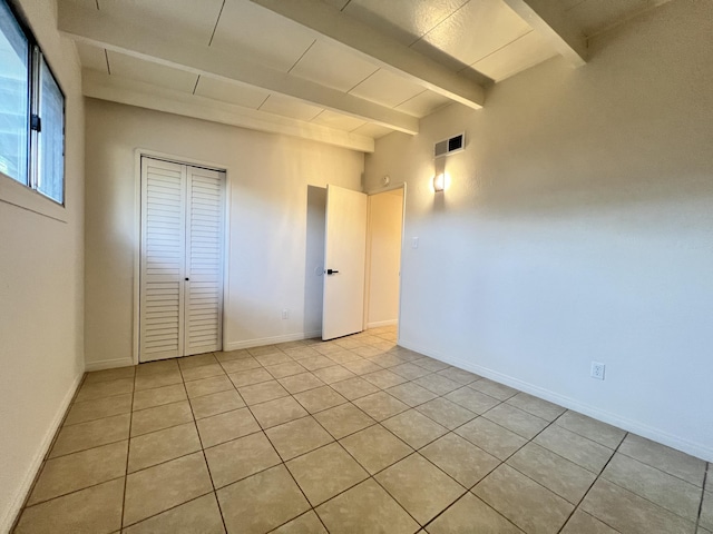 unfurnished bedroom featuring beam ceiling, light tile patterned flooring, and a closet