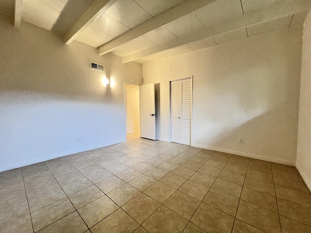 tiled spare room featuring beamed ceiling