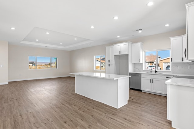 kitchen with white cabinetry, light hardwood / wood-style floors, stainless steel dishwasher, a kitchen island, and a tray ceiling