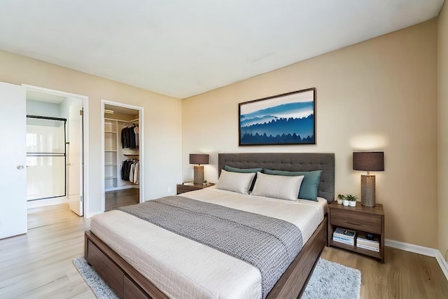 bedroom with baseboards, a spacious closet, a closet, and light wood-style floors