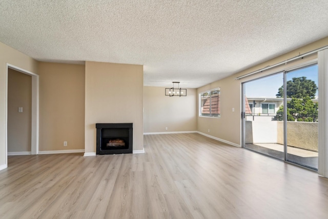 unfurnished living room with a fireplace, an inviting chandelier, a textured ceiling, light wood-type flooring, and baseboards