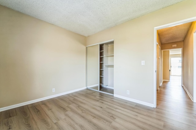 unfurnished bedroom with baseboards, a textured ceiling, a closet, and light wood-style floors