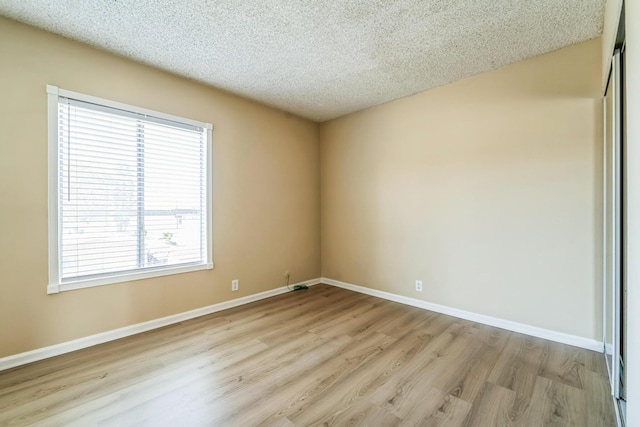 spare room with a textured ceiling, wood finished floors, and baseboards