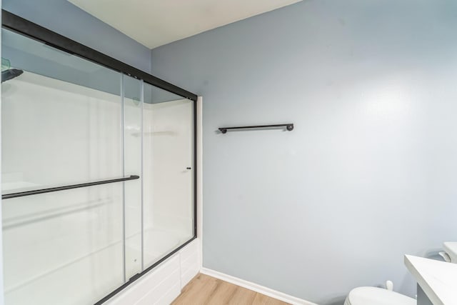 bathroom featuring toilet, enclosed tub / shower combo, vanity, wood finished floors, and baseboards